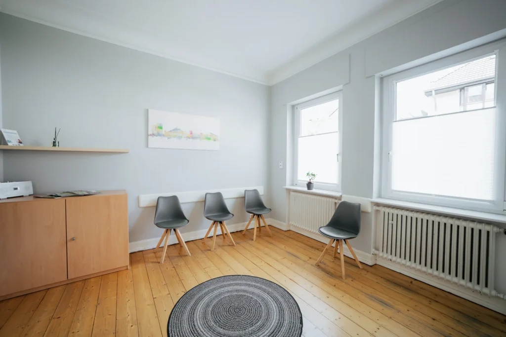 Heller, einladender Raum mit Stühlen, Holzboden und Kunstwerk an der Wand, ideal für Gespräche und Beratungen.